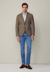 Braun kariertes Blazer mit Spitzenklappen, zwei Knöpfen und Klappentaschen, kombiniert mit einem hellblauen Hemd und hellblauen Jeans. Braune Loafers.