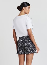 Top bianco a maniche corte con dettaglio in raso nero sulla spalla, abbinato a pantaloni corti neri con una stampa a macchie bianche astratte.
