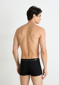 Boxer-briefs noirs avec une ceinture de marque, design ajusté et tissu lisse. Modèle vu de dos, portant des manches courtes et sans motifs visibles.