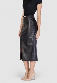 Falda de lápiz de cuero negro con una abertura frontal, diseño ajustado, textura suave y cintura alta, combinada con tacones altos nude.