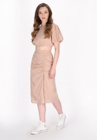 Twee-delig outfit met een gekorte blouse met puffmouwen en een knie-lange, gerimpelde rok van een zachte beige stof, gecombineerd met witte high-top sneakers.