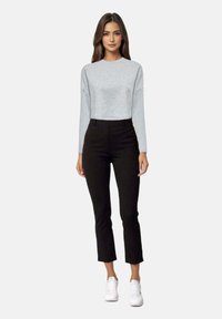 Maglietta grigia chiara a maniche lunghe abbinata a pantaloni neri aderenti e corti e sneakers bianche, creando un outfit casual e rilassato.