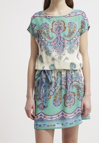 Lyhythihainen, kevyt mekko, jossa on paisleikuvio turkoosissa, kermanvalkoisessa ja purppurassa, joustava vyötärö ja solmittu nauhakiinnitys.