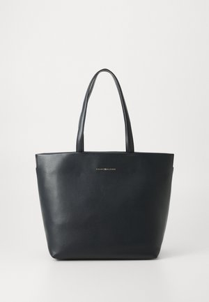 Námořnická kožená taška přes rameno s dvojitými dlouhými uchy; má hladký povrch a zlaté logo na přední straně. Obdélníkový tvar, minimalistický design.