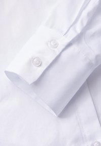 Polsino di camicia in cotone bianco con due bottoni trasparenti, texture liscia e dettagli cuciti con cura lungo il bordo.