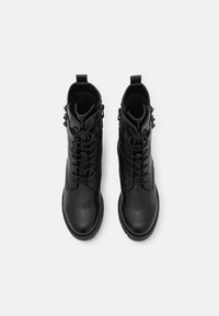 Botas de cuero negras hasta el tobillo con un acabado suave, que cuentan con un diseño de cordones, cremalleras y acentos metálicos con tachuelas en los lados.