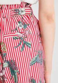 Tissu à rayures rouges et blanches à motifs floraux, avec une taille ceinturée, présentant des feuilles vertes et diverses fleurs, texture lisse, coupe ajustée.