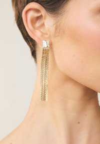 Gold geometric drop earrings with a textured finish and long, cascading fringe. They feature a rectangular stud attachment.