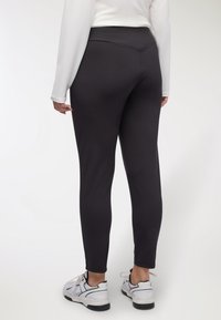 Czarne, dopasowane legginsy wykonane z elastycznego materiału o gładkiej fakturze, z wysokim stanem i bezszwowym designem. Nosi się je z białymi trampkami.
