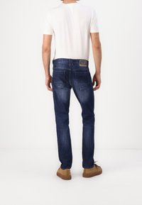 Mörkblå denimjeans med rak passform, med en läderpatch på baksidan av midjan och subtila blekningsdetaljer. Bärs med en vit T-shirt.