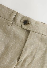 Pantaloni di lino beige con un sottile motivo a righe, caratterizzati da un bottone marrone e una vita sartoriale. Texture liscia e design strutturato.