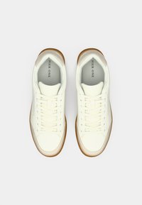 Ζευγάρι λευκά sneakers χαμηλού ύψους με μπεζ λεπτομέρειες και καφέ σόλες, σε άποψη από πάνω σε λευκό φόντο.