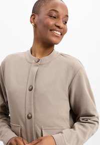 Beige, langemouwen, knoopjack met een ronde kraag, textuurstof, twee voorzakken en grote houten knopen.