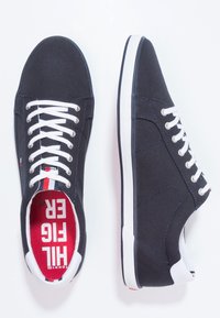 Scarpe da ginnastica in tela blu navy con lacci bianchi e suole in gomma. L'interno presenta accenti rossi e bianchi con il testo "HILFIGER". Texture liscia.