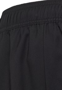 Schwarzer Stoff mit strukturierter Oberfläche, ausgestattet mit einem elastischen Bund und genähten Falten, die ein glattes, einheitliches Finish zeigen.