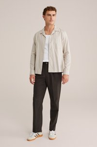 Camicia button-up color beige chiaro con tasca, pantaloni eleganti neri e sneakers bianche con dettagli beige. Tessuto morbido, vestibilità informale.