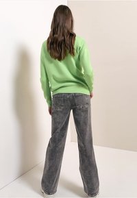 Maglione verde chiaro con finitura testurizzata, abbinato a jeans grigi a vita alta e gamba larga, con effetto slavato e tasche posteriori classiche.