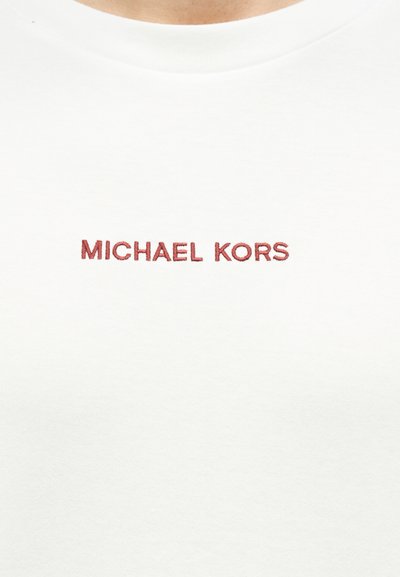 Бяла тениска с кръгло деколте и червен бродиран текст "MICHAEL KORS" в центъра на гърдите.