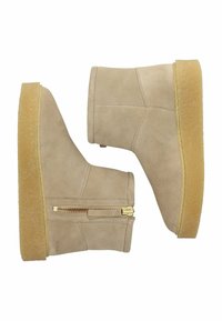 Botas de ante beige hasta el tobillo con una suela texturizada, detalle de cremallera lateral y un diseño elegante y minimalista. Presentan una superficie suave y aterciopelada.