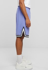 Lys lilla træningsshorts med sort og hvid kant, med en markant vinklet nederkant, parret med hvide sneakers og ankelsokker.