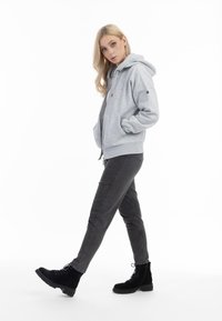 Grijze ritssluiting hoodie met een capuchon, twee voorzakken en geribbelde manchetten, gedragen met zwarte skinny jeans en zwarte veterschoenen.
