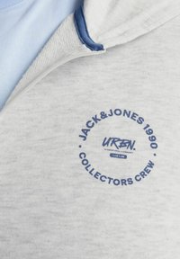 Grå crew-neck sweatshirt med en blå detalje ved kraven. Har et cirkulært logo trykt med mørkeblå tekst på forsiden. Tekstur af bomuldsblanding.