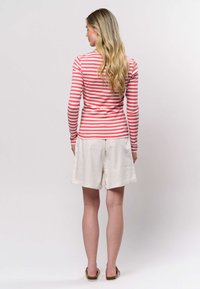 Pika varrukaga punase ja valge triibuline särk, mida kannavad põlveni kreemjad lühikesed püksid, millel on lõdva istuvus ja üles rullitud ääred.