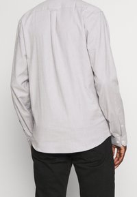 Lichtgrijze longsleeve shirt met een button-down kraag, subtiele textuur en een afgeronde zoom; voorzien van manchetten met één knop en een rugplooi.