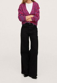 Cárdigan a rayas en fucsia y azul, con escote en V y ajuste corto. Pantalones vaqueros de pierna ancha negros, con cintura alta y cierre de botón clásico.