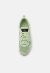 Sneaker verde chiaro con punta perforata, collo imbottito e lacci bianchi, visto dall'alto su uno sfondo bianco.