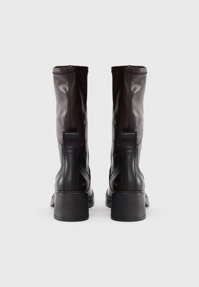 Bottes en cuir marron montantes, à bout rond, avec un talon bloc robuste et des coutures décoratives à l'arrière et sur les côtés.
