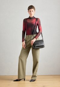 Haut long à manches transparentes rouge et noir associé à un pantalon beige ample. Sac à main noir avec rabat et talons aiguilles noirs.