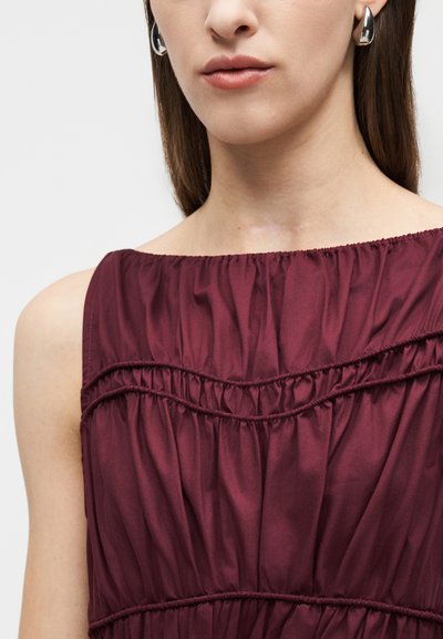 Κοντινό πλάνο γυναίκας που φοράει ασημένια σκουλαρίκια κρίκους και μπουστάκι βουργουνδίας χωρίς μανίκια με οριζόντιες ραφές.