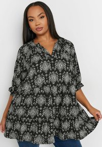 Czarna i biała bluzka w wzory o luźnym kroju, z dekoltem w serek i podwiniętymi rękawami. Posiada zwiewny fason z motywami florystycznymi.