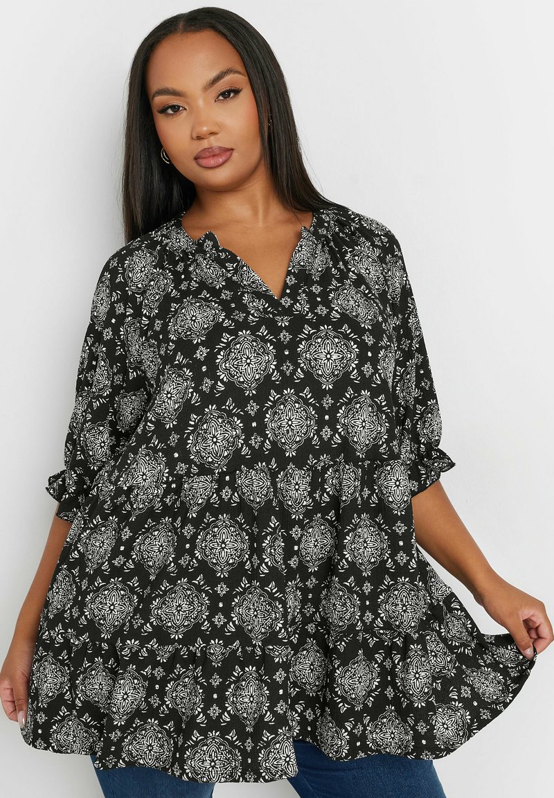 Czarna i biała bluzka w wzory o luźnym kroju, z dekoltem w serek i podwiniętymi rękawami. Posiada zwiewny fason z motywami florystycznymi.