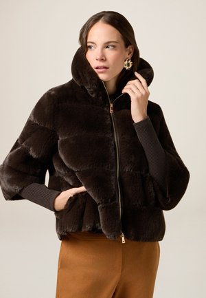 Brązowa kurtka z sztucznego futra z wysokim kołnierzem, suwakiem i szerokimi rękawami. Posiada poziome szwy i miękką, teksturowaną powierzchnię.