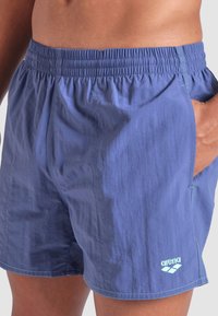 Pantaloni da nuoto blu realizzati in un tessuto leggero e testurizzato, con vita elastica, tasche laterali e un logo blu chiaro.