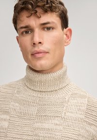 Beżowy sweter z golfem, zdobiony teksturowanymi wzorami, ściągaczem przy kołnierzu i dzianym wzorem. Zbliżenie na tkaninę i linię szyi.