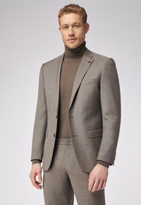 Szary garniturowy żakiet z klapami, brązowy golf i dopasowane spodnie. Posiada subtelne faktury i brązowe akcenty guzików.