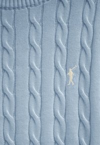 Lyseblåt kabelstrikket stof med en lille hvid broderet figur af en person, der holder en golfkølle.