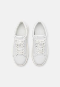 Sneakers bianchi in pelle con una texture liscia, caratterizzati da una forma arrotondata, chiusura con lacci e design minimalista. Logo visibile sulla linguetta.