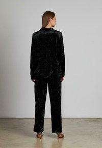 Conjunto de lounge de terciopelo negro que incluye una camisa de manga larga con cuello y pantalones holgados, que exhibe una textura suave y un brillo sutil.