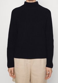 Schwarzer gerippter Strickrollkragenpullover mit Raglanärmel und geradem Saum, kombiniert mit hellbeigen Shorts.