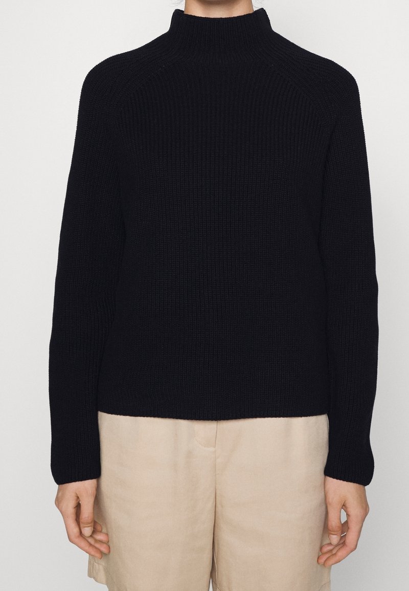 Schwarzer gerippter Strickrollkragenpullover mit Raglanärmel und geradem Saum, kombiniert mit hellbeigen Shorts.