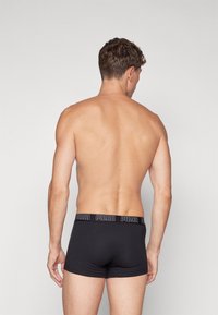 Schwarze Baumwoll-Boxershorts mit einem Puma-Logo-Bund, die eine enge Passform und glatte Textur aufweisen, von hinten gezeigt.