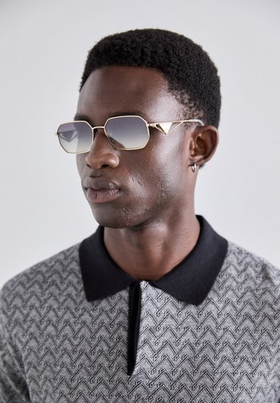 Guldindfattede oktagonale solbriller med gradient grå linser, parret med en mønstrede sort og grå polo skjorte med sort krave.