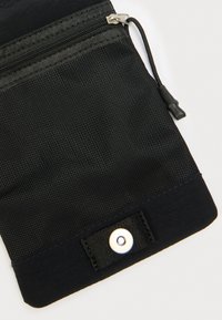 Μαύρο πορτοφολάκι με φερμουάρ και διαχωριστικό από δίχτυ, με λείο ύφασμα στο κάτω μέρος και κούμπωμα με κουμπί. Υφή στην επιφάνεια και λεπτομέρεια με κορδόνι.