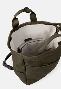 Sac à main matelassé vert olive avec fermeture éclair. Comprend un intérieur beige, une poche zippée, deux poignées et une bandoulière réglable.