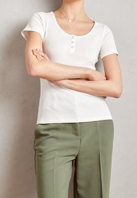 Valkoinen ribbineulottu lyhythihainen paita, jossa on pyöreä pääntie ja kolmen napin läppä. Yhdistetty vaaleanvihreisiin räätälöityihin housuihin.