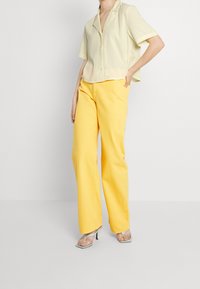 Chemise jaune clair à manches courtes avec une patte de boutonnage, associée à un pantalon jaune à jambes larges et des sandales vertes à talons. Design simple et contemporain.